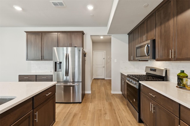 kitchen featuring light stone countertops, appliances with stainless steel finishes, tasteful backsplash, dark brown cabinets, and light hardwood / wood-style floors