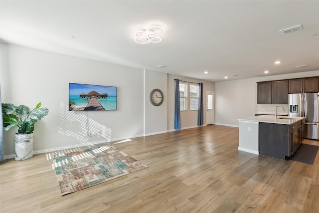 kitchen with dark brown cabinetry, stainless steel fridge with ice dispenser, a kitchen island with sink, and light wood-type flooring