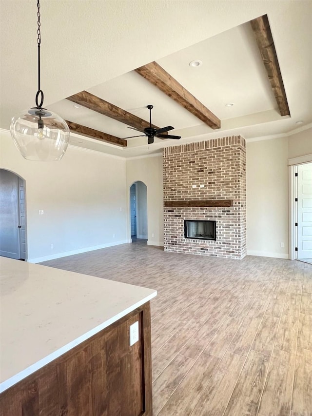 unfurnished living room with a ceiling fan, light wood finished floors, a fireplace, arched walkways, and beamed ceiling