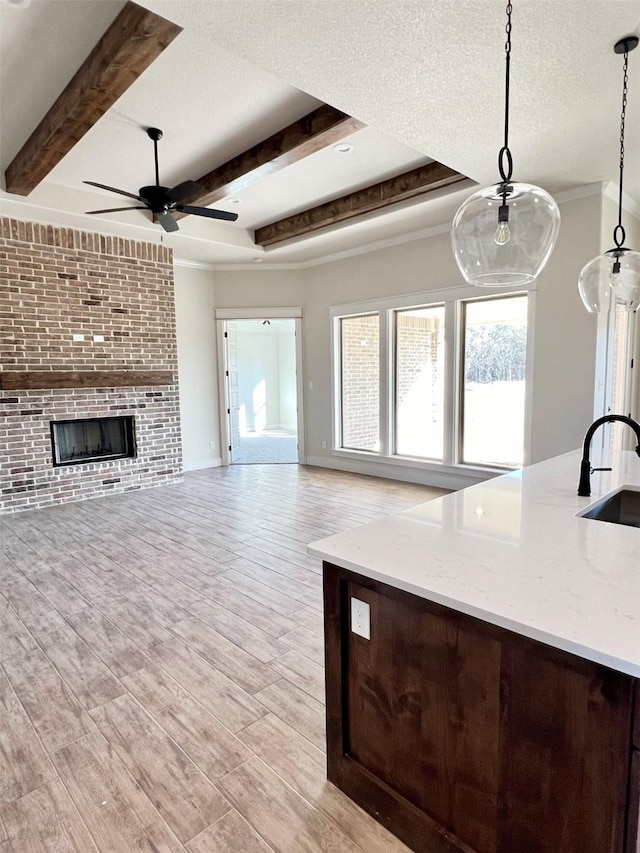 unfurnished living room featuring a sink, light wood-style floors, a textured ceiling, and a brick fireplace