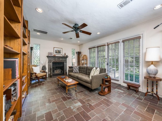 living room featuring stone finish floor, visible vents, a fireplace, and ceiling fan