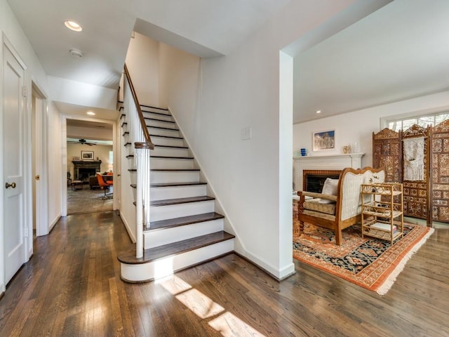 stairs with hardwood / wood-style floors, a brick fireplace, and ceiling fan