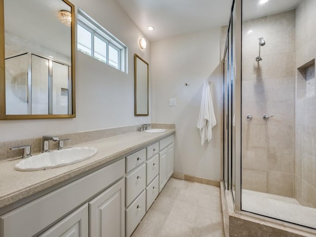 full bathroom featuring double vanity, a stall shower, baseboards, and a sink