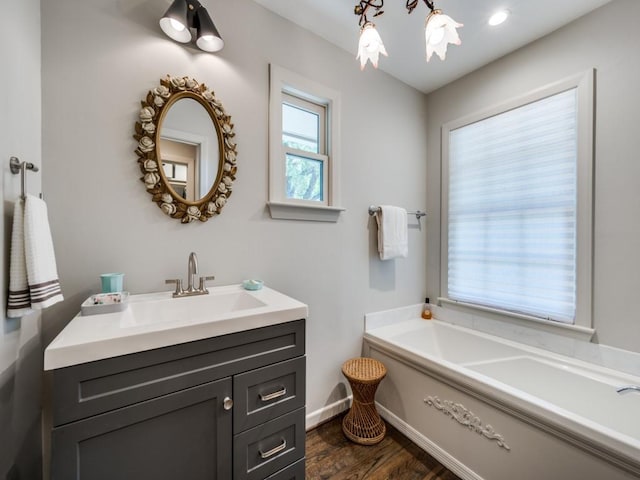 full bathroom with a garden tub, vanity, baseboards, and wood finished floors