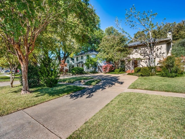 view of front of property with concrete driveway, a chimney, and a front yard