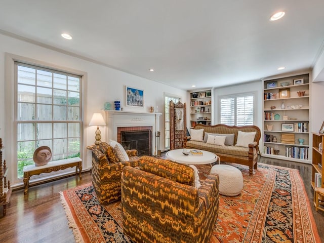 living room featuring built in shelves, crown molding, a fireplace, and dark hardwood / wood-style floors