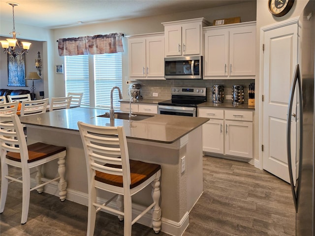 kitchen featuring sink, stainless steel appliances, an island with sink, decorative light fixtures, and white cabinets