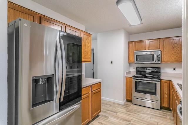 kitchen with a textured ceiling, stainless steel appliances, and light hardwood / wood-style floors