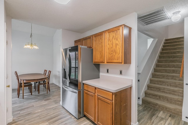 kitchen featuring light hardwood / wood-style flooring, stainless steel fridge, a chandelier, pendant lighting, and a textured ceiling