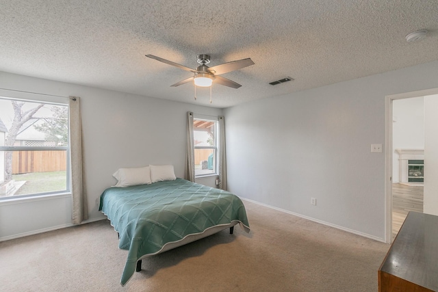 bedroom with ceiling fan, light colored carpet, and a textured ceiling