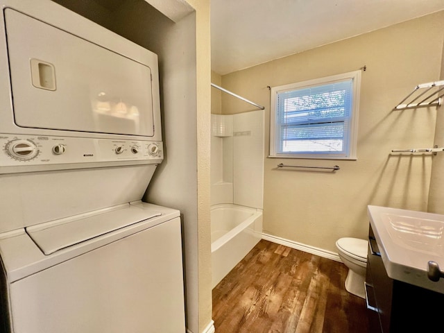 full bathroom with stacked washing maching and dryer, vanity, shower / washtub combination, wood-type flooring, and toilet