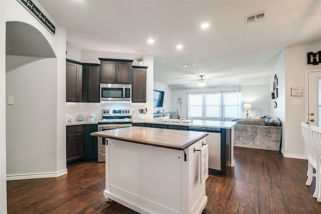 kitchen with dark brown cabinetry, a center island, stainless steel appliances, dark wood-type flooring, and kitchen peninsula