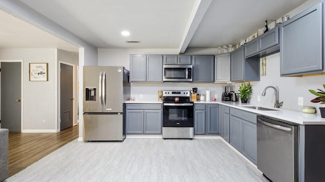 kitchen featuring sink, light hardwood / wood-style flooring, gray cabinets, appliances with stainless steel finishes, and beam ceiling