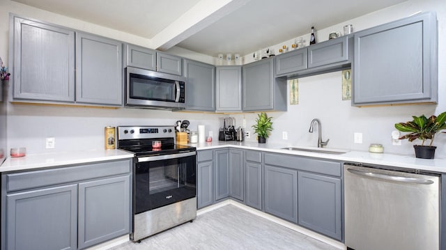 kitchen featuring sink, gray cabinets, light wood-type flooring, appliances with stainless steel finishes, and beam ceiling