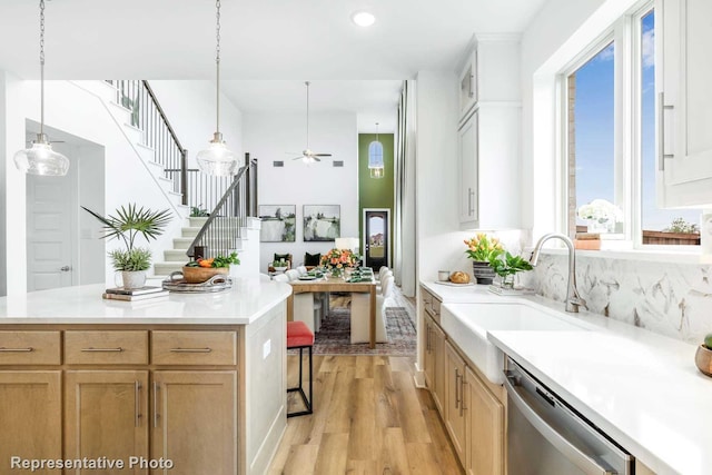 kitchen featuring white cabinetry, sink, stainless steel dishwasher, light hardwood / wood-style floors, and decorative light fixtures