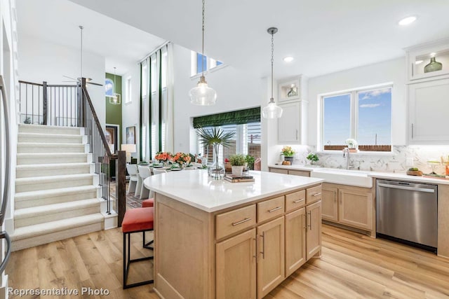 kitchen featuring light brown cabinetry, backsplash, sink, dishwasher, and a kitchen island