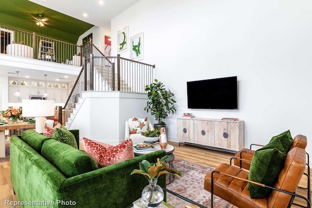 living room with ceiling fan, light hardwood / wood-style flooring, and a towering ceiling