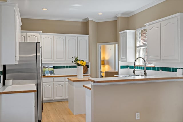 kitchen with stainless steel fridge, crown molding, white cabinets, and sink