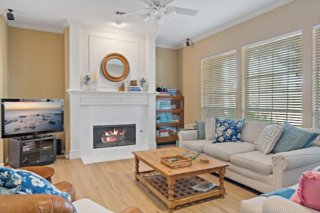 living room featuring a tile fireplace, ceiling fan, ornamental molding, and light wood-type flooring