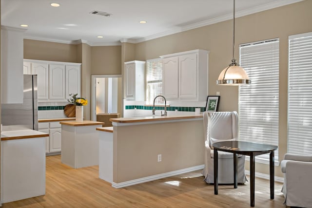 kitchen featuring a center island, hanging light fixtures, ornamental molding, white cabinetry, and stainless steel refrigerator