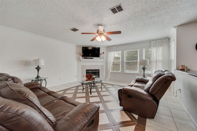 living room with ceiling fan, ornamental molding, a fireplace, and a textured ceiling