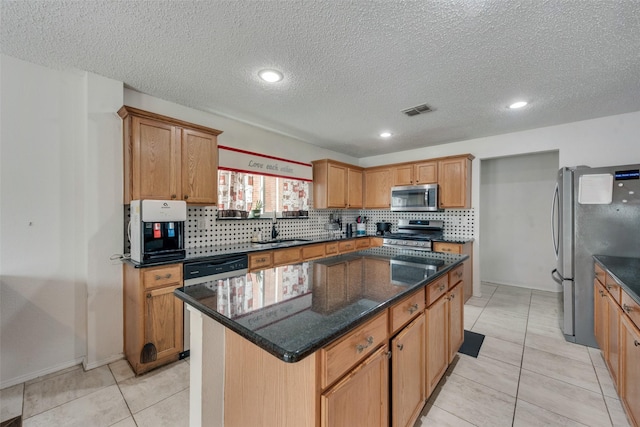 kitchen featuring sink, appliances with stainless steel finishes, a kitchen island, dark stone counters, and backsplash