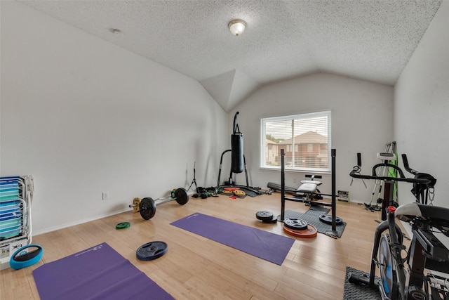 workout area with vaulted ceiling, a textured ceiling, and light hardwood / wood-style flooring