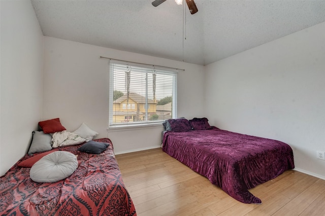 bedroom with vaulted ceiling, light hardwood / wood-style floors, and a textured ceiling