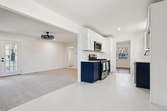 kitchen with light carpet, stainless steel appliances, blue cabinetry, decorative backsplash, and white cabinets