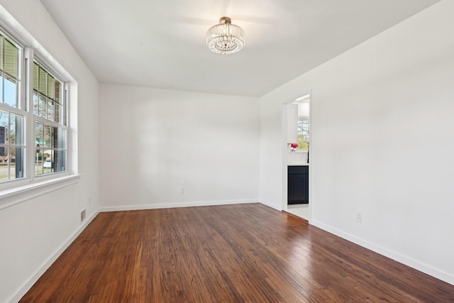 empty room featuring a notable chandelier and dark wood-type flooring