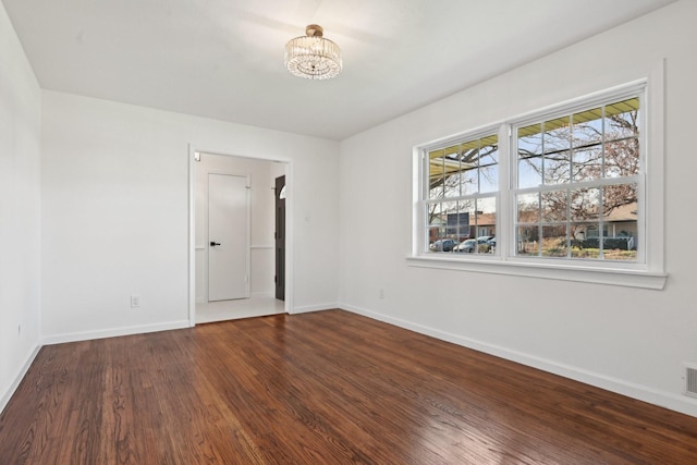 unfurnished room featuring a notable chandelier and dark wood-type flooring