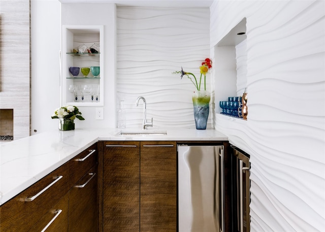 bar with dark brown cabinetry, light stone countertops, sink, and fridge