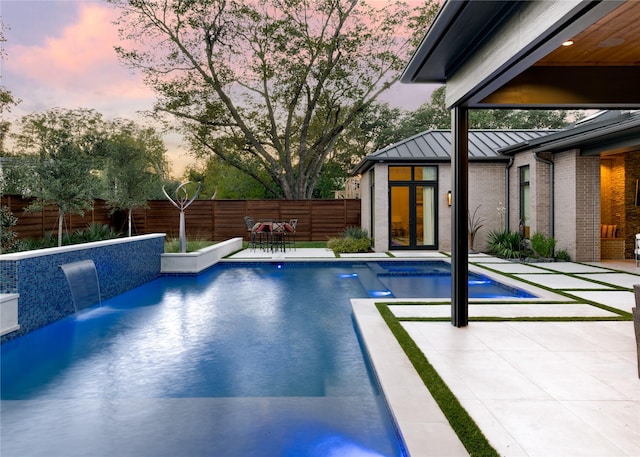 pool at dusk with pool water feature and a patio area