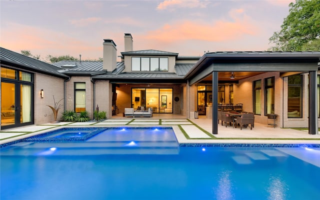 back house at dusk featuring an outdoor living space, ceiling fan, a patio area, and a pool with hot tub