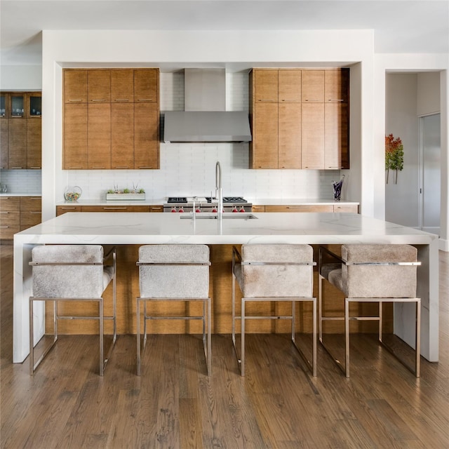 kitchen with a kitchen bar, backsplash, wall chimney exhaust hood, and dark wood-type flooring