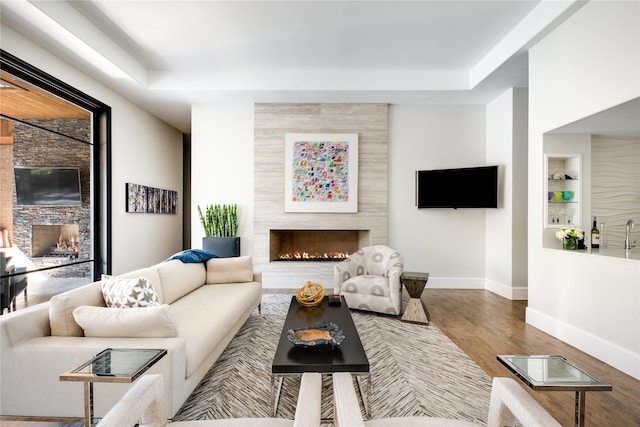 living room with a tile fireplace, built in features, and hardwood / wood-style flooring