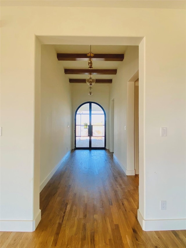 empty room with beamed ceiling, french doors, and wood-type flooring