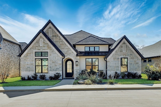 french country inspired facade featuring a standing seam roof, a lawn, and stucco siding