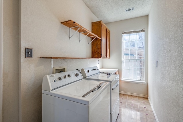 laundry area featuring washing machine and dryer, a wealth of natural light, cabinets, and a textured ceiling