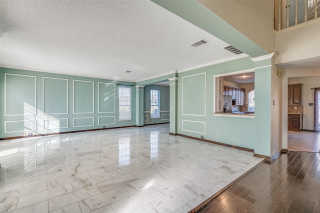 unfurnished living room featuring ornate columns, a textured ceiling, and ornamental molding