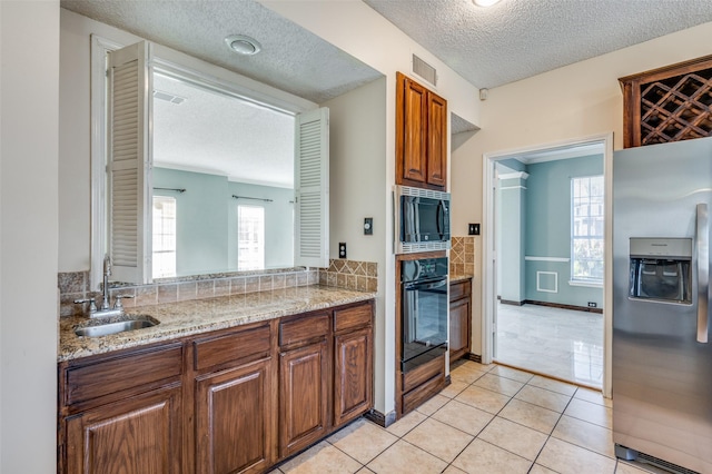 kitchen with sink, a textured ceiling, appliances with stainless steel finishes, light tile patterned flooring, and light stone counters