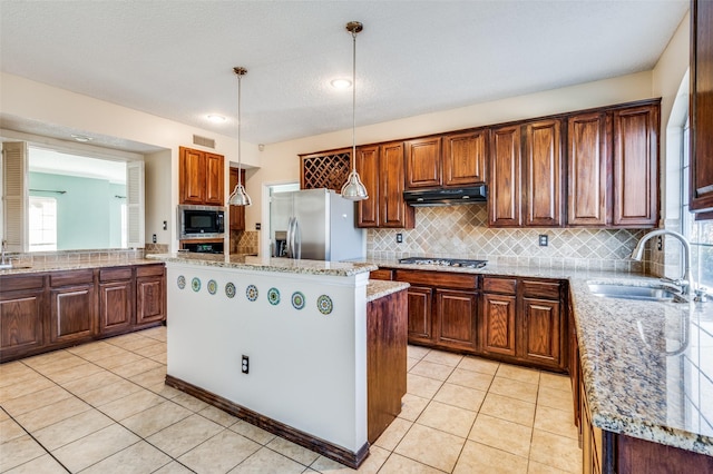 kitchen with sink, stainless steel appliances, light stone counters, pendant lighting, and a kitchen island