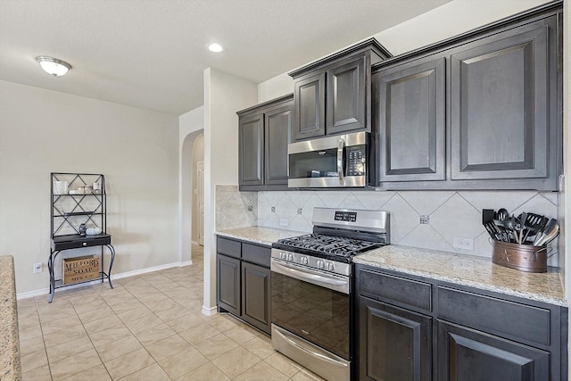 kitchen with appliances with stainless steel finishes, tasteful backsplash, light stone counters, and light tile patterned flooring