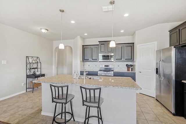 kitchen with decorative light fixtures, light tile patterned flooring, stainless steel appliances, and a kitchen island with sink