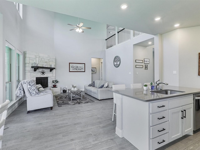 kitchen with a kitchen island with sink, sink, a fireplace, light hardwood / wood-style floors, and white cabinetry