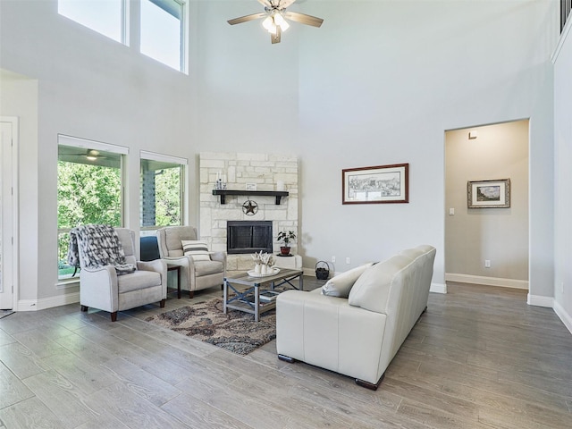 living room with a stone fireplace, plenty of natural light, a towering ceiling, and light hardwood / wood-style floors