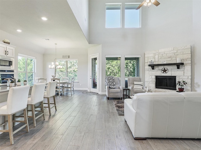 living room featuring ceiling fan with notable chandelier, a stone fireplace, and a high ceiling