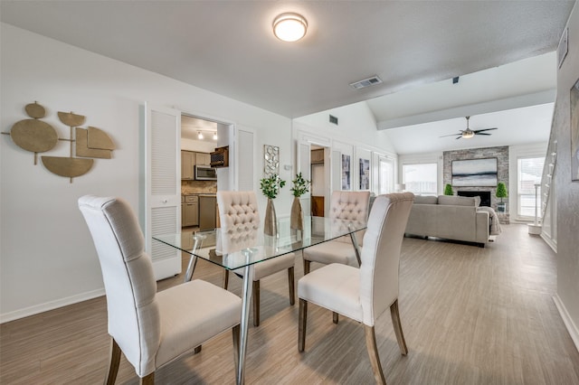 dining room with a fireplace, hardwood / wood-style flooring, ceiling fan, and lofted ceiling