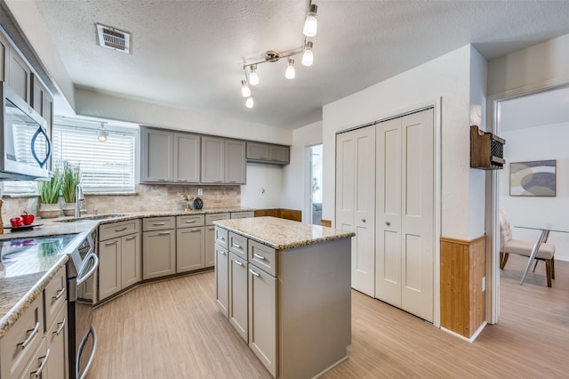 kitchen featuring appliances with stainless steel finishes, a center island, a textured ceiling, and light hardwood / wood-style flooring