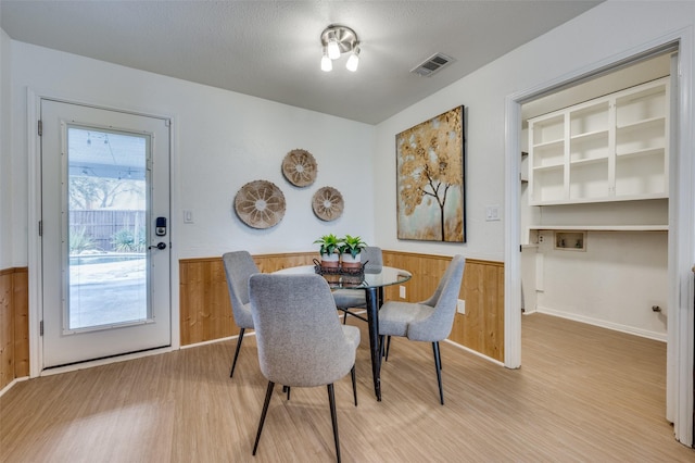 dining room with wooden walls, light hardwood / wood-style flooring, and a textured ceiling